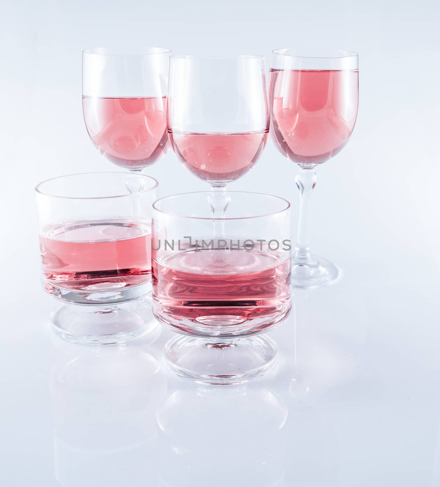 Rosè wine in stemmed glasses on white background with reflection