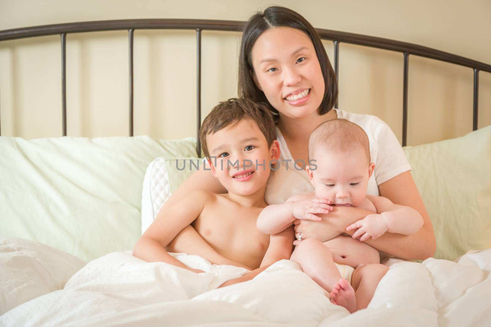 Young Mixed Race Chinese and Caucasian Baby Boys Laying In Bed with Their Mother.