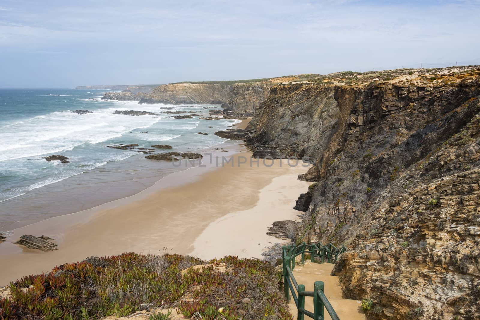 green staircase to the beach and wild ocean splash water to the rocks of the west coast of Portugal