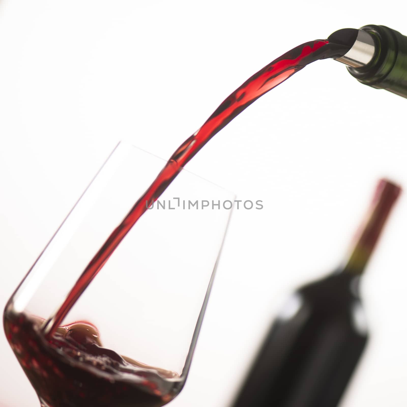 Pouring red wine into wineglass from green bottle, white background