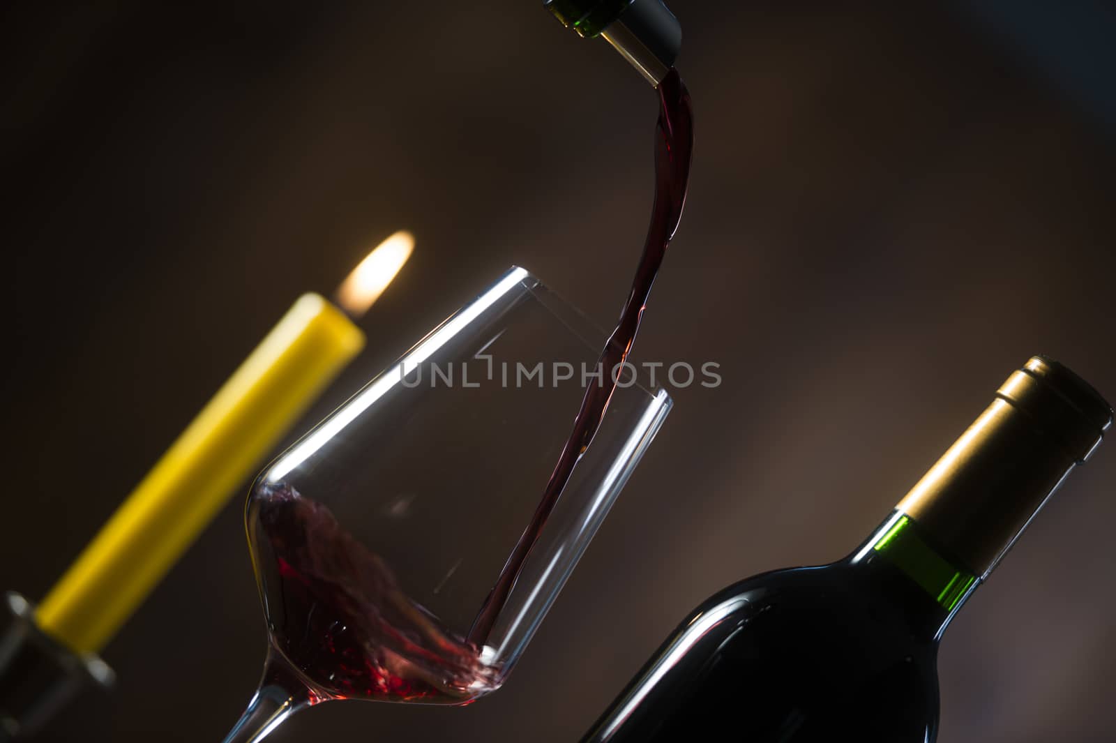 Pouring red wine into wineglass from green bottle, brown background