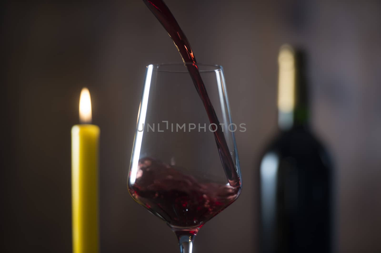 Pouring red wine into wineglass from green bottle, brown background