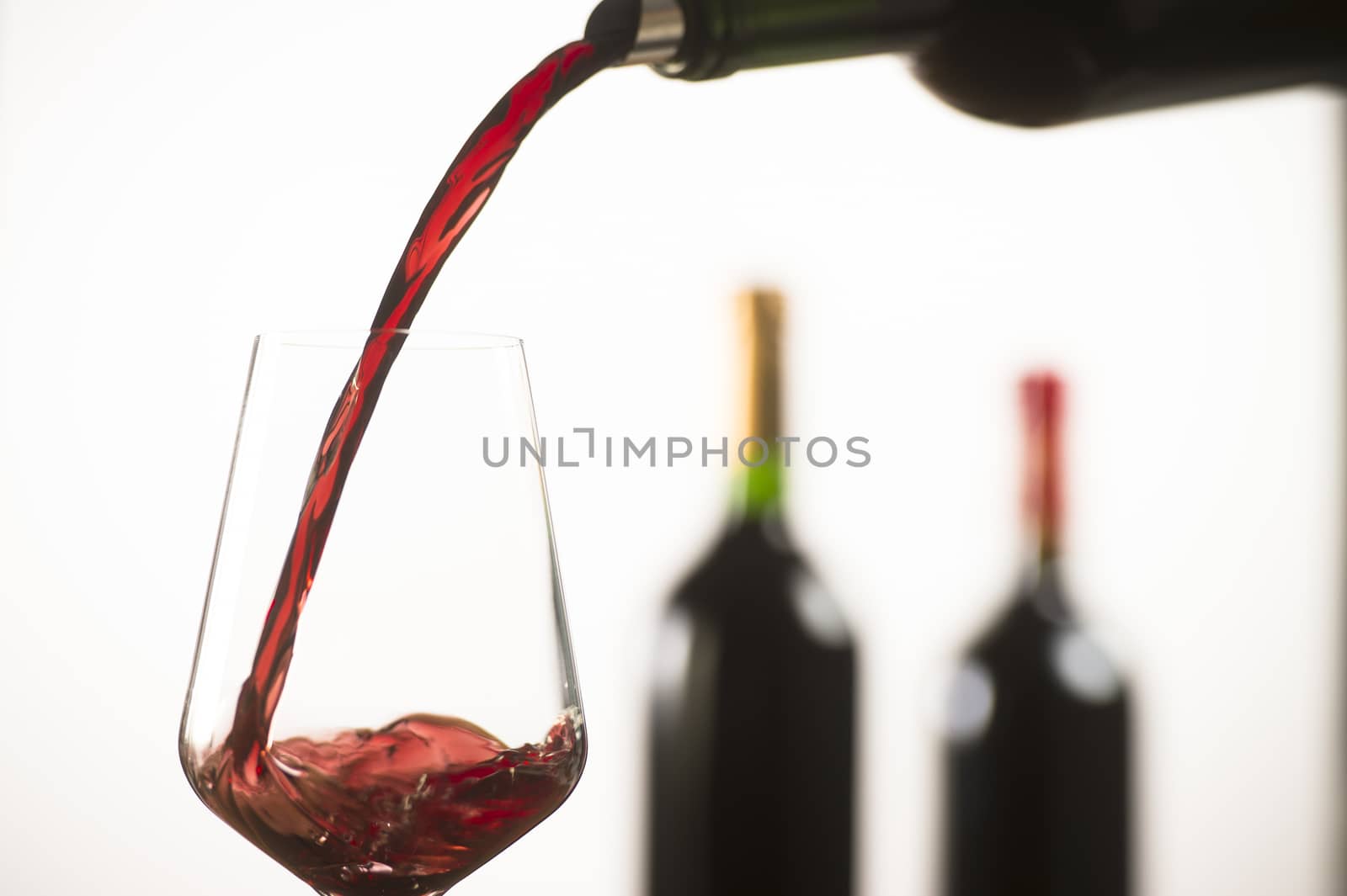 Pouring red wine into wineglass from green bottle, white background