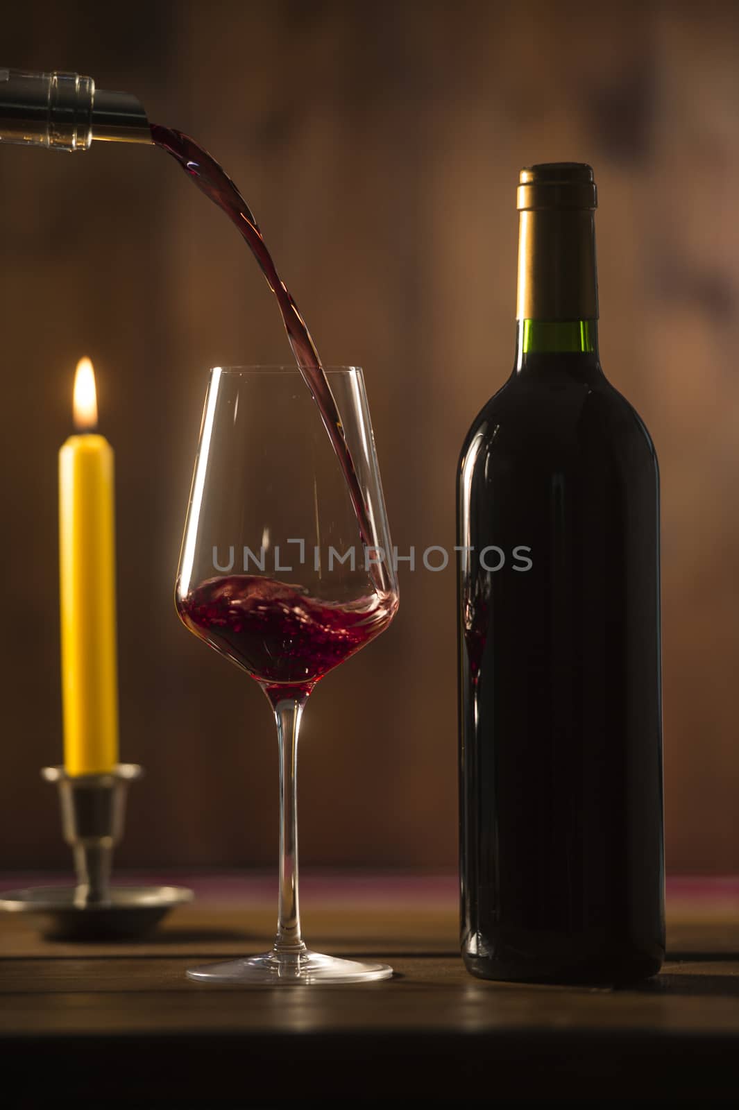 Pouring red wine into wineglass from green bottle, brown background