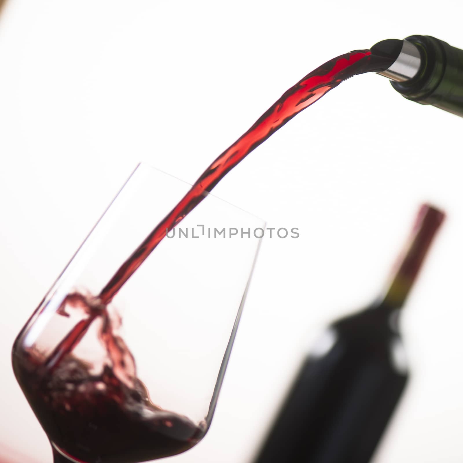 Pouring red wine into wineglass from green bottle, white background