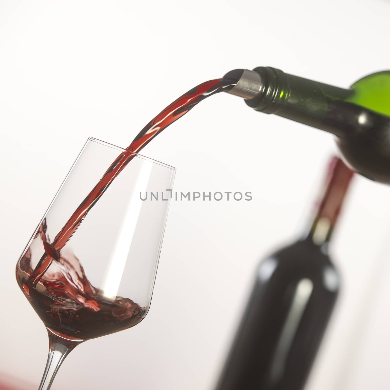 Pouring red wine into wineglass from green bottle, white background