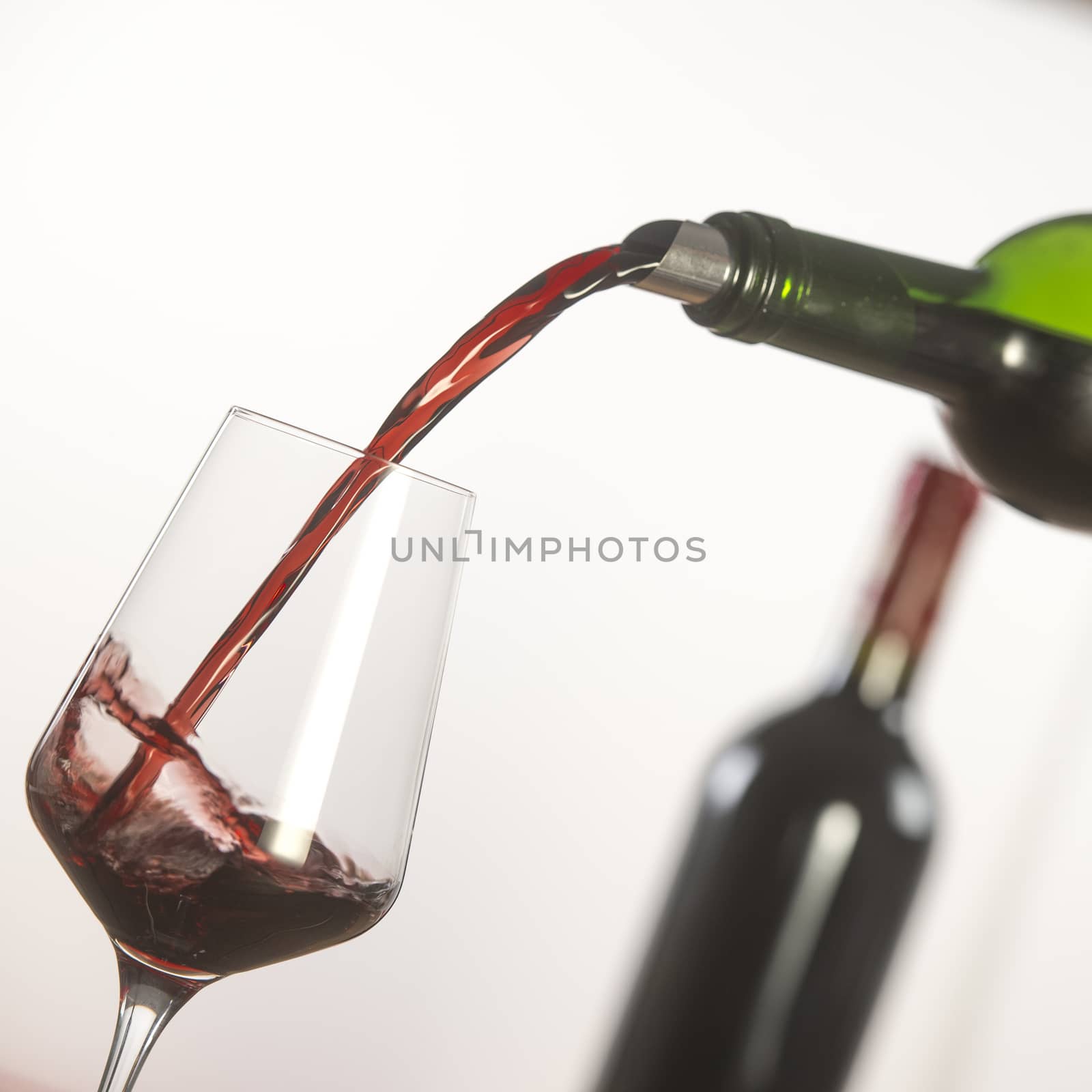 Pouring red wine into wineglass from green bottle, white background