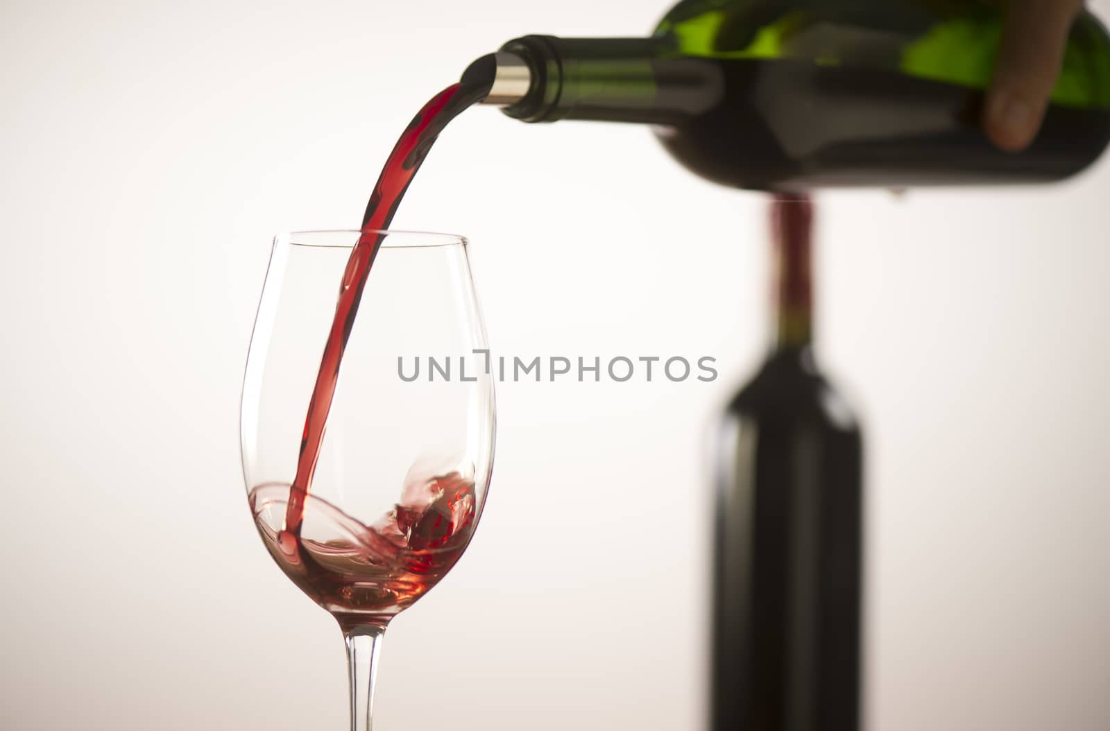 Pouring red wine into wineglass from green bottle, white background