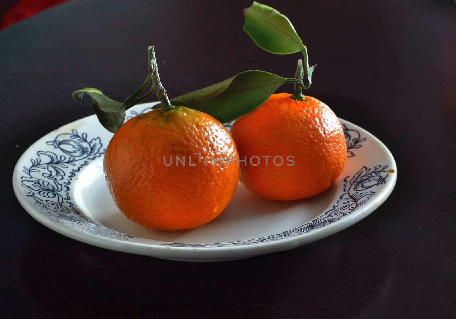 two orange tangerine with leafs on a white plate