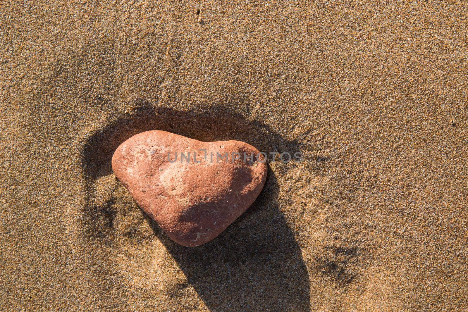 Heart shaped stone on the sand of a beach by YassminPhoto