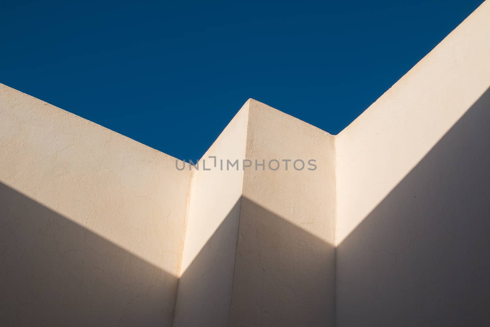 Detail of an architecture, enlightened on the edge by the sunlight, darker in the shadows. Deep blue sky in the background.