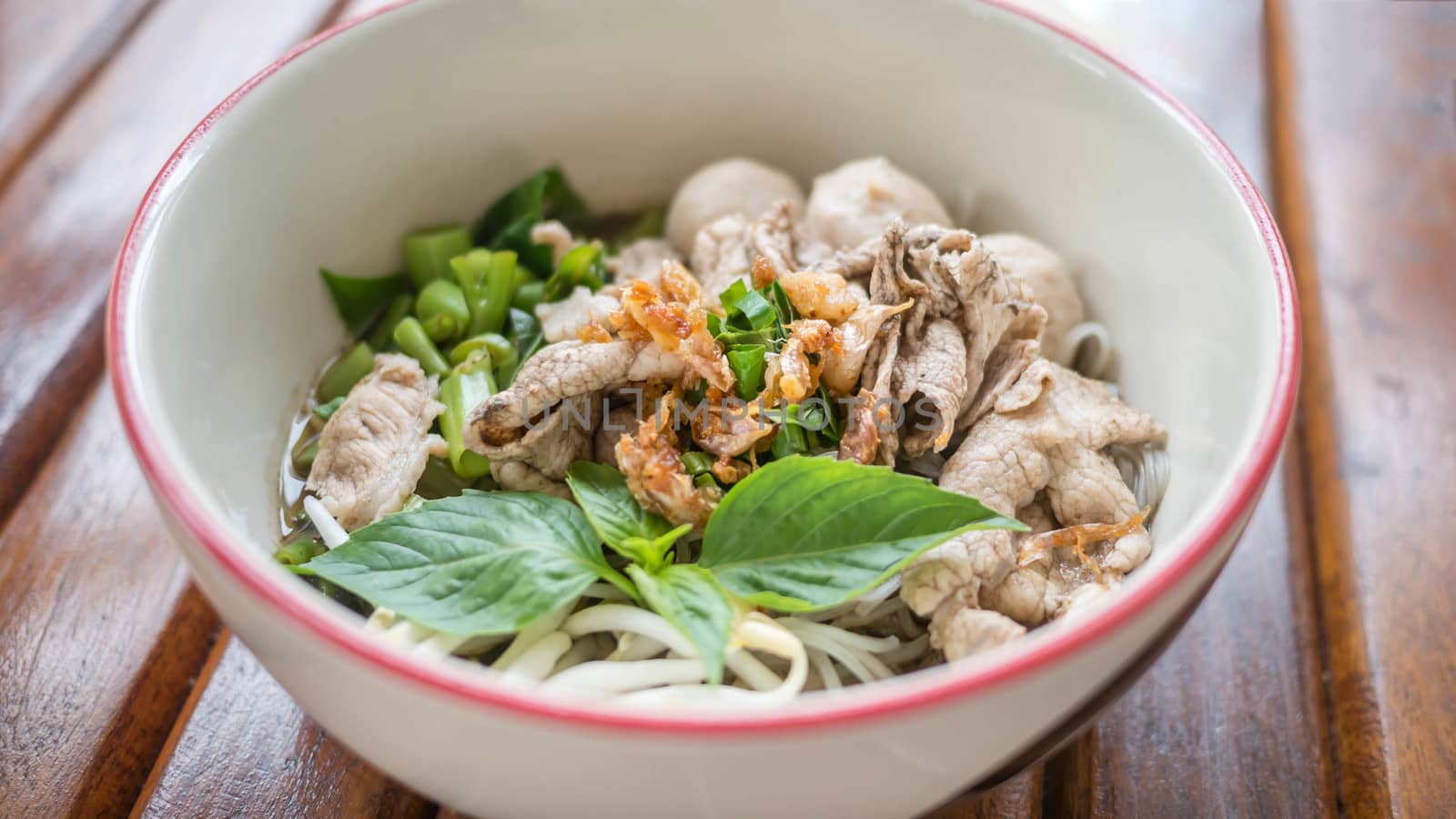 Asian white noodles with pork and vegetables in bowl over wooden background