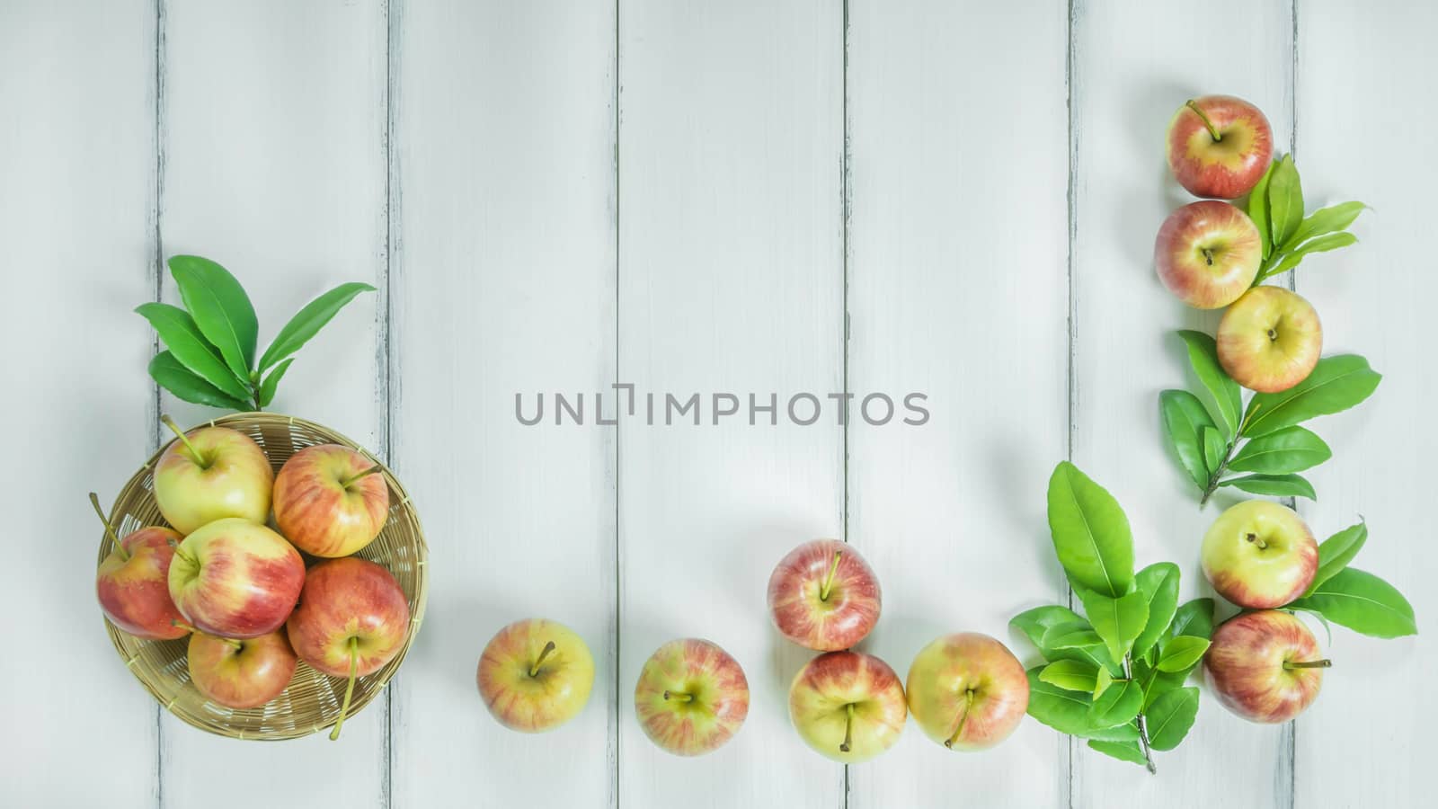 Top view red and yellow apple with leaves and  bamboo basket on  white wooden background with free space for text