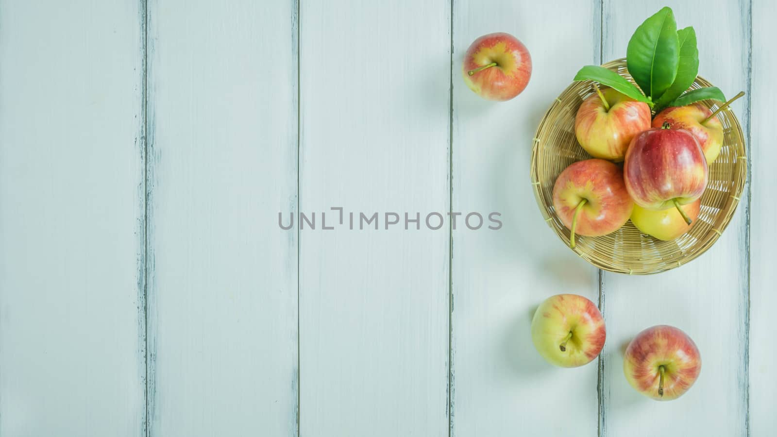 Top view red and yellow apple with leaves and  bamboo basket on  white wooden background with free space for text