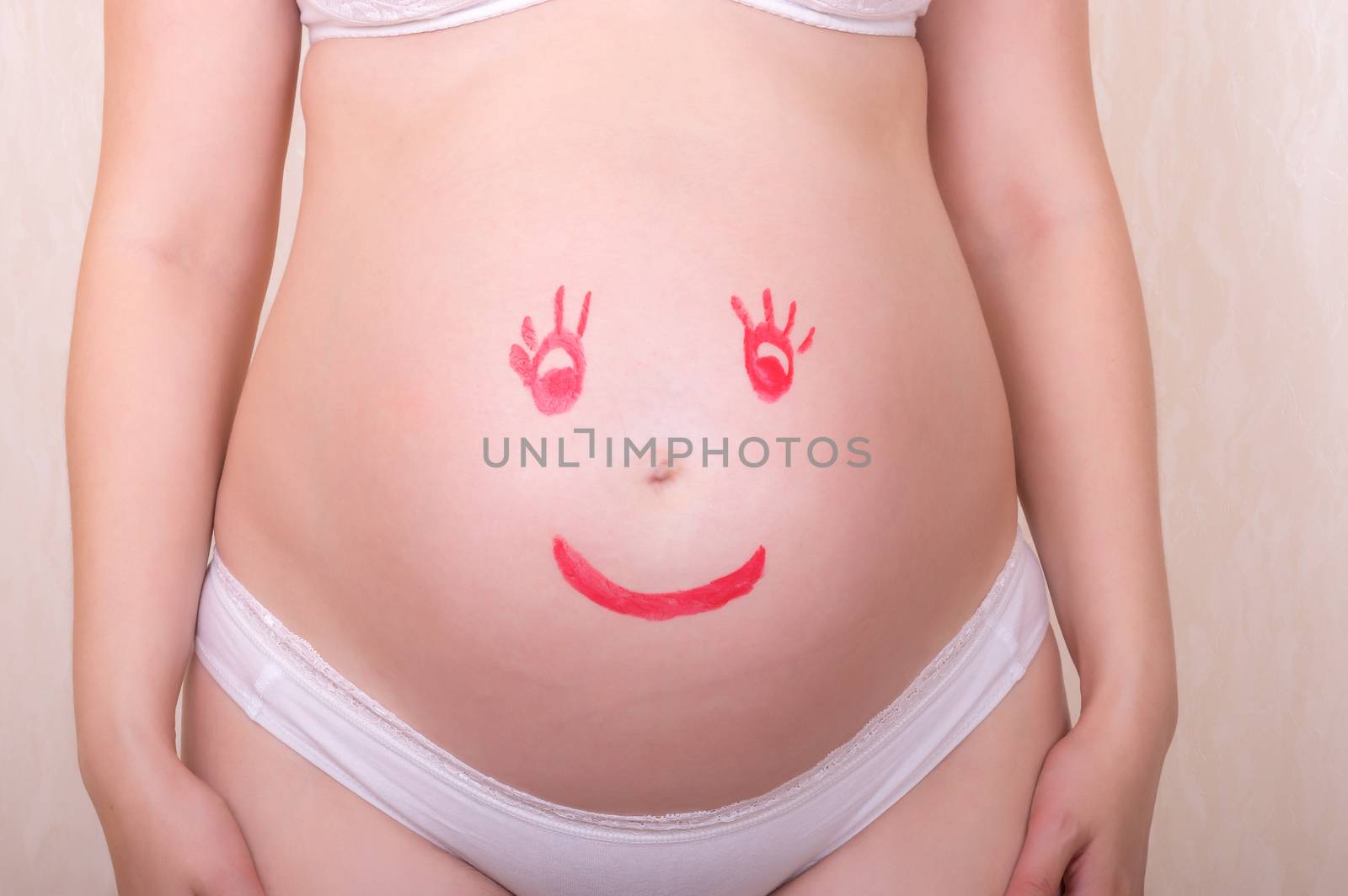 Face drawn in lipstick on a stomach of the pregnant woman