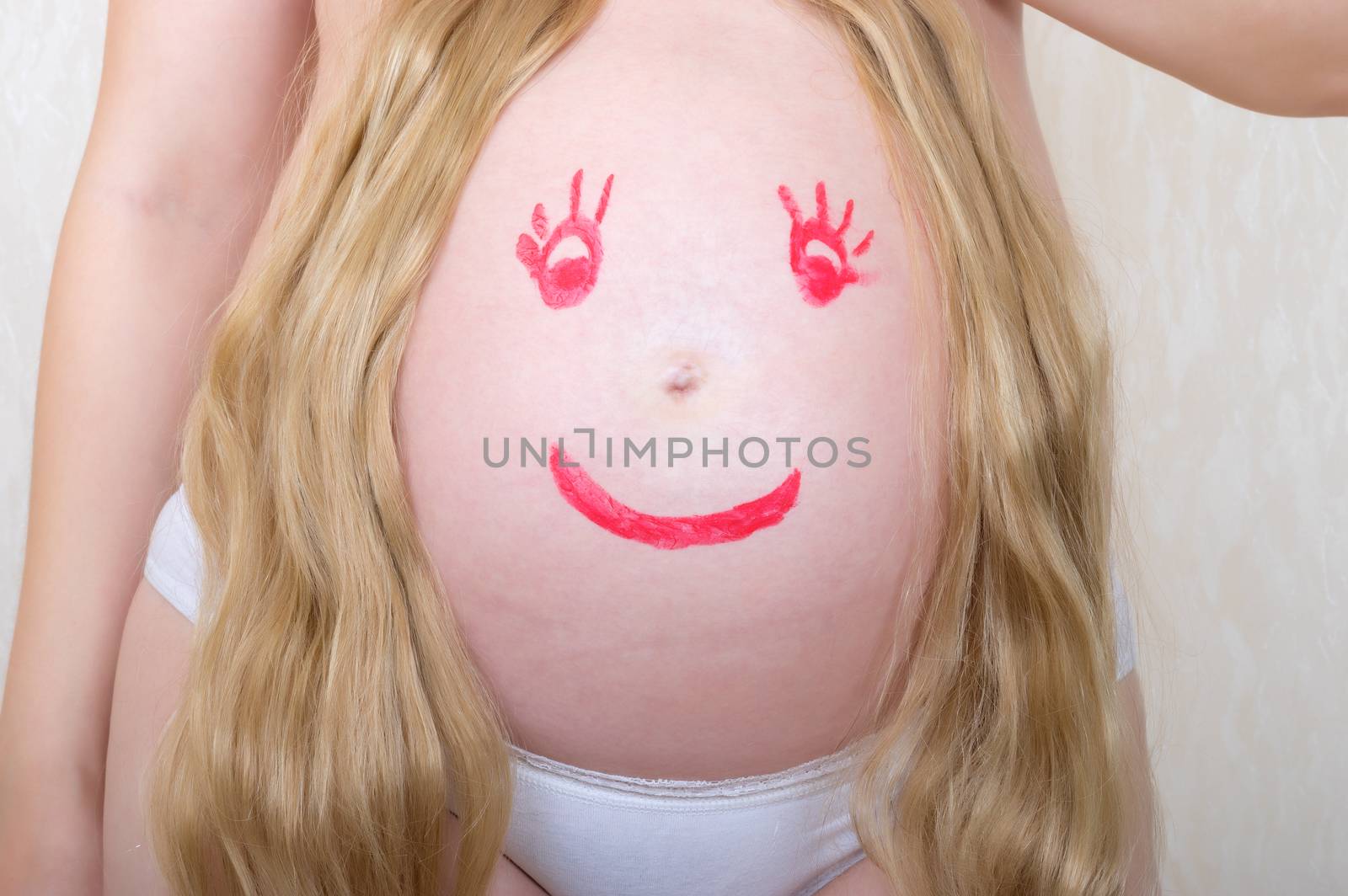 Face drawn in lipstick on a stomach of the pregnant woman