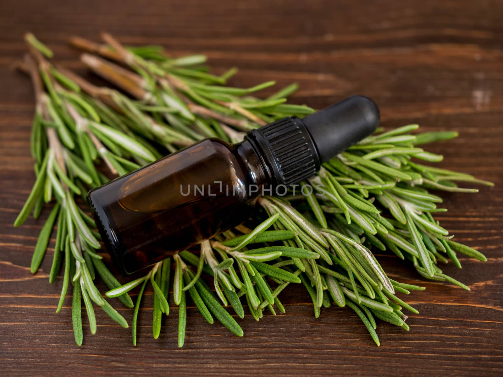 Rosemary essential oil in dark glass bottle and fresh rosemary on dark wooden background. Top view or flat lay