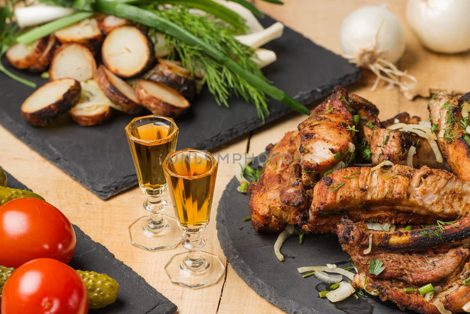 Fried meat, potatoes, greens, vegetables on slate plates and two shot glasses with cognac in style a rustic