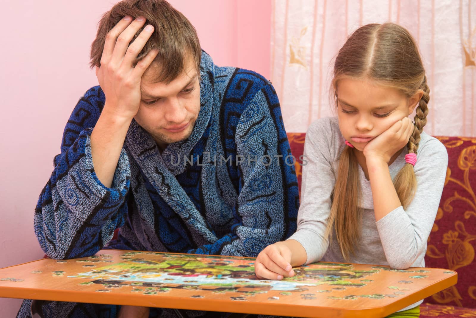 My daughter collects a picture from puzzles, tired dad sitting next to her and tells