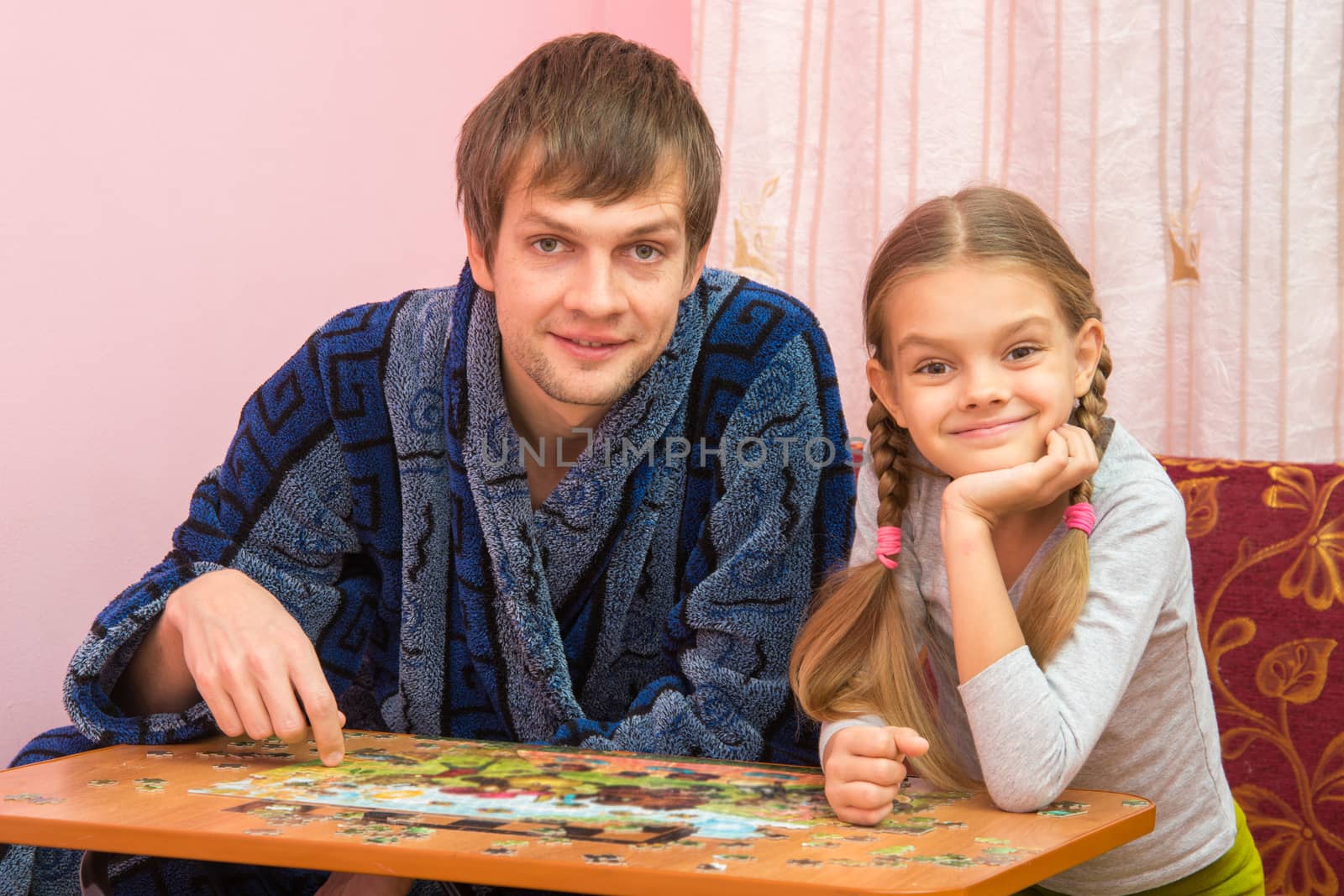 Dad and daughter in the frame looked sitting at the table and collecting puzzles