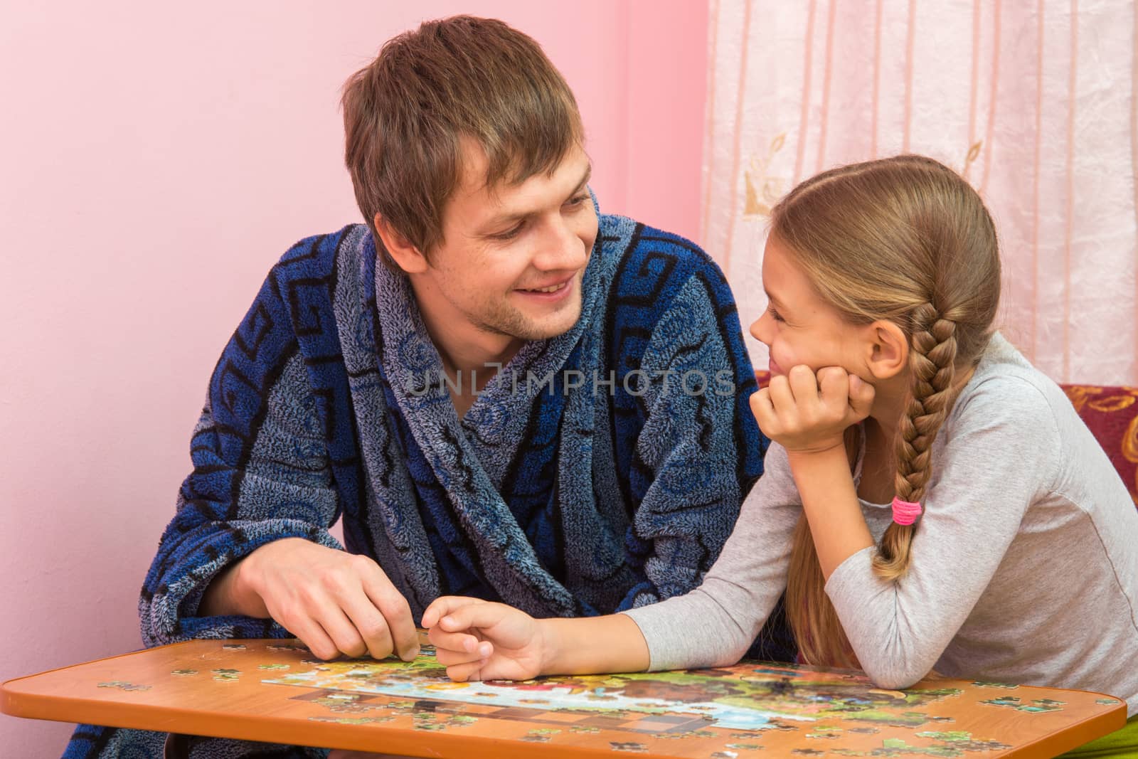 Father and daughter looked at each other collecting puzzle elements