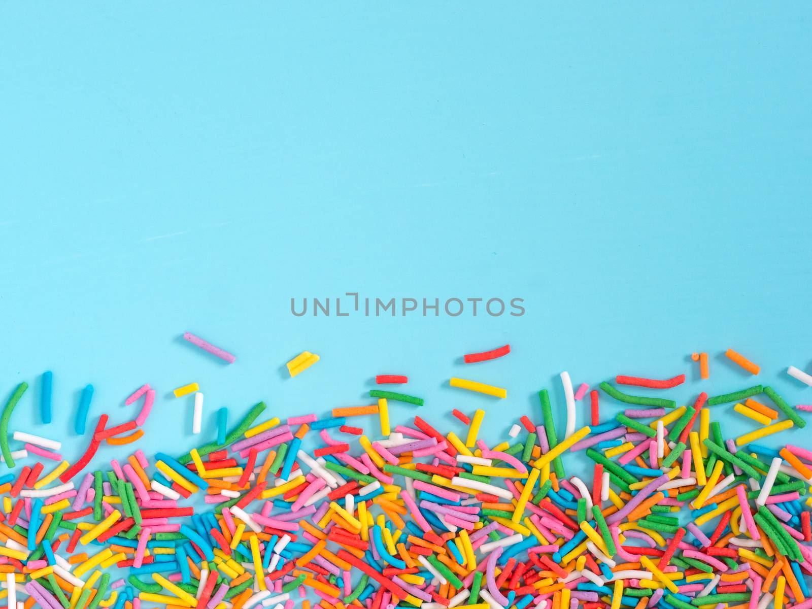 Border frame of colorful sprinkles on blue background with copyspace. Top view or flat lay