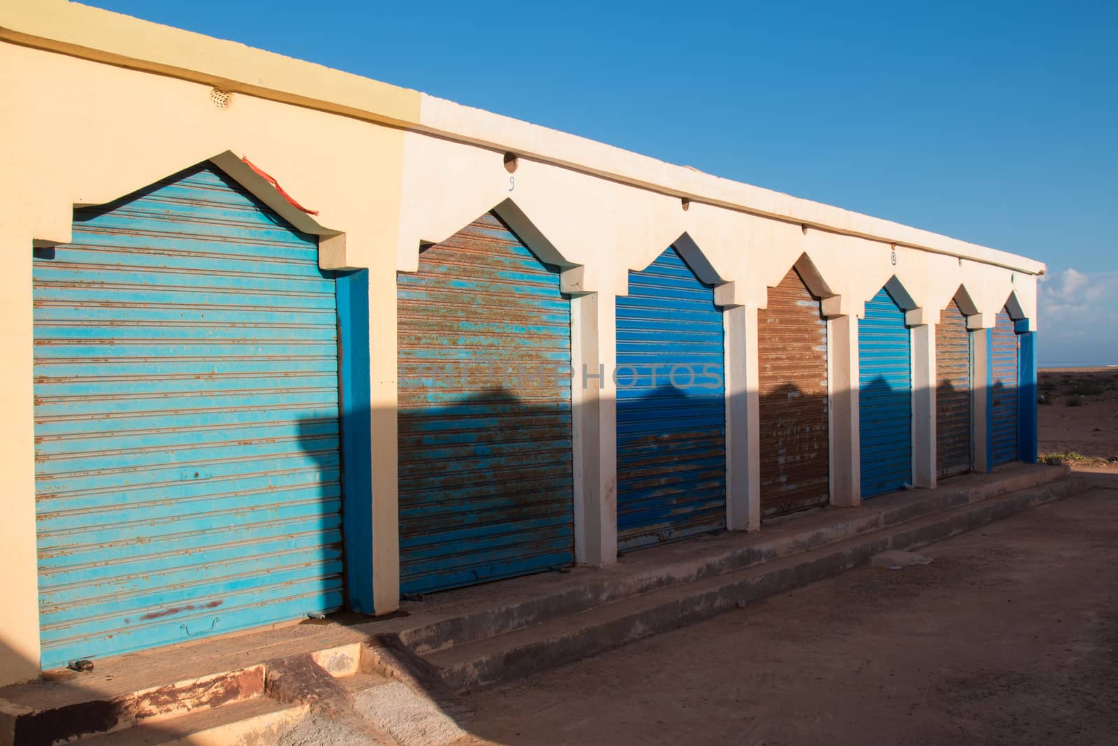 Block of shops, still closed with roller blinds. Traditional arabian style. Yellow facade enlightened by the morning sunlight. Sidi Ifni beach, Morocco