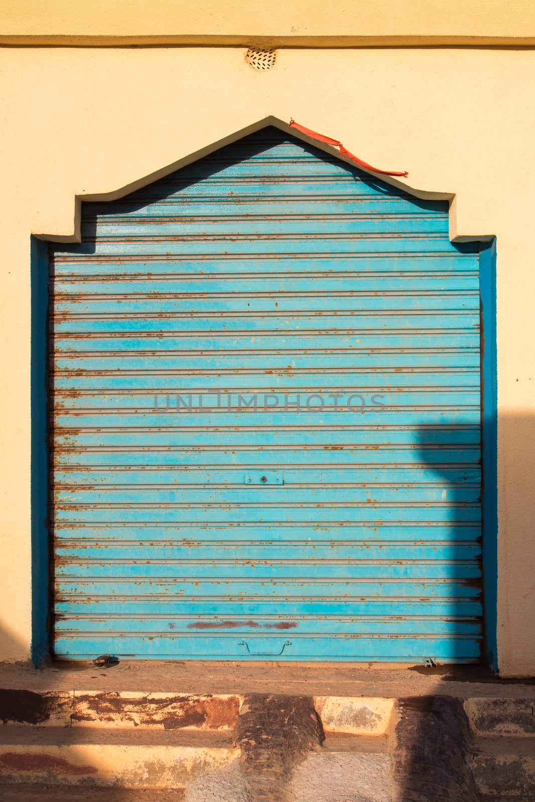 Detail of a shop, still closed with a blue roller blind. Traditional arabian style. Yellow facade enlightened by the morning sunlight. Sidi Ifni, Morocco