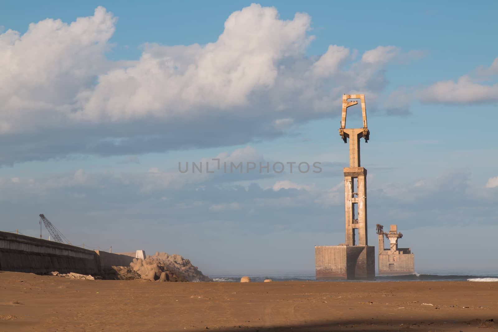 View on a part of a port in coastal city Sidi Ifni, Morocco. Sandy beach in the foreground. Early morning sunlight, intense clouds on the sky.