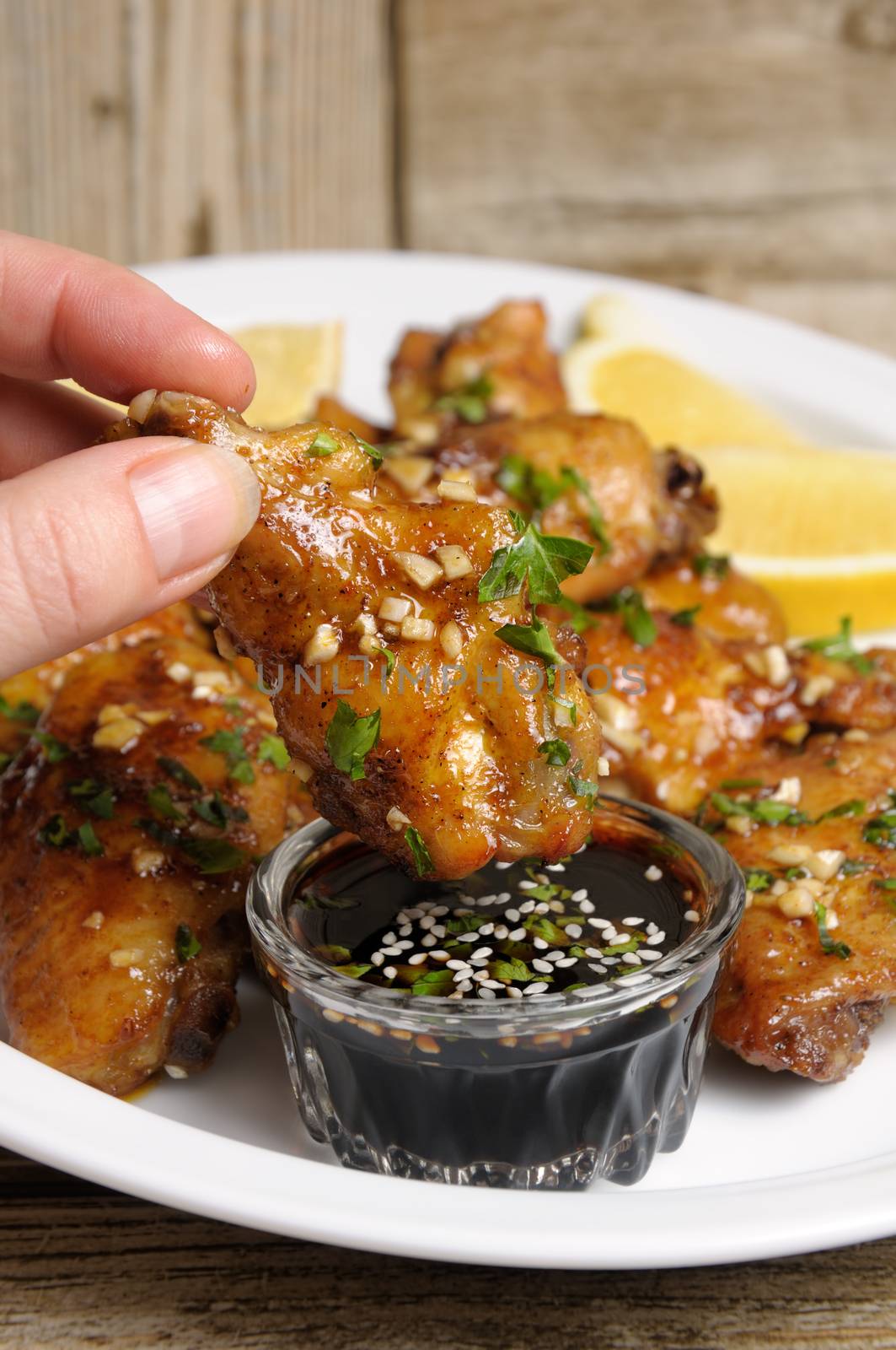 Fried chicken wing in ginger garlic marinade with herbs in hand over soy sauce