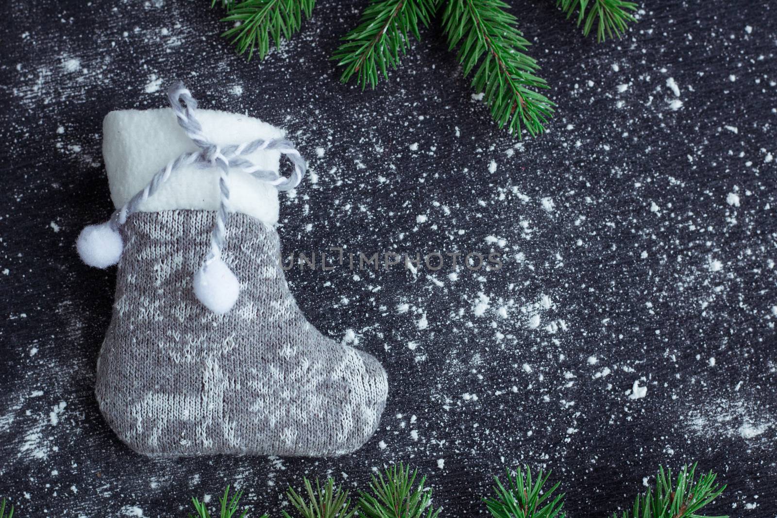 Christmas and New Year winter holiday snowbound composition of grey stocking on black space background with green fir tree branches