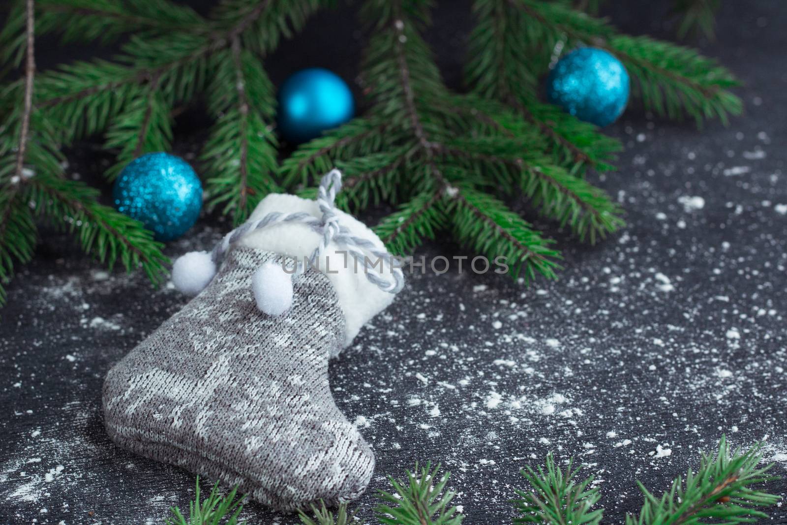 Christmas and New Year winter holiday snowbound composition of grey stocking on black space background with green fir tree branches and blue balls ornament