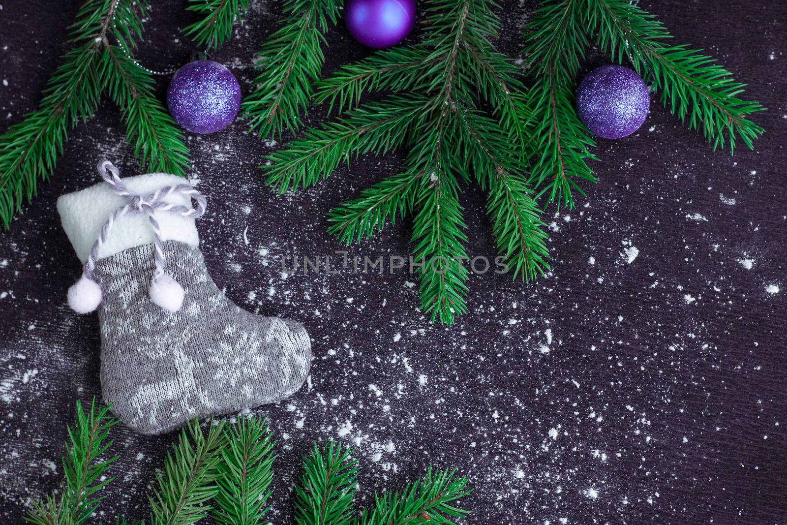 Christmas and New Year winter holiday snowbound composition of grey stocking on black space background with green fir tree branches and purple balls ornament