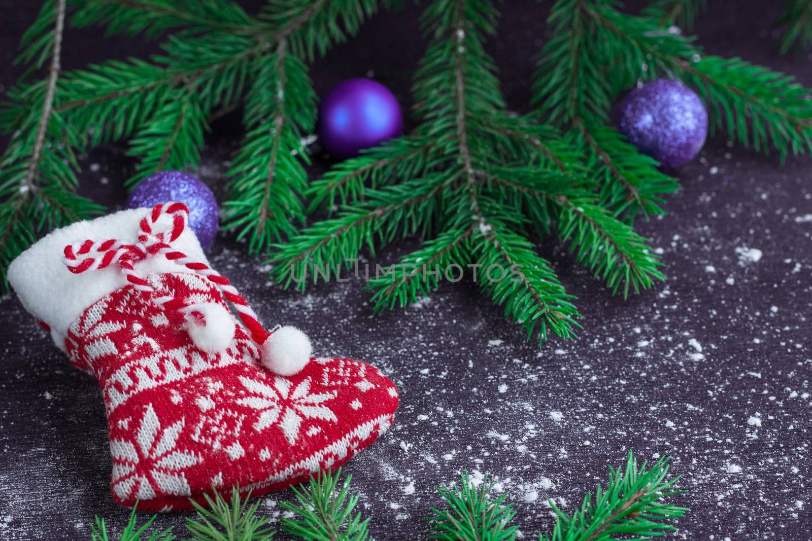 Christmas and New Year winter holiday snowbound composition of red stocking on black space background with green fir tree branches and purple balls ornament
