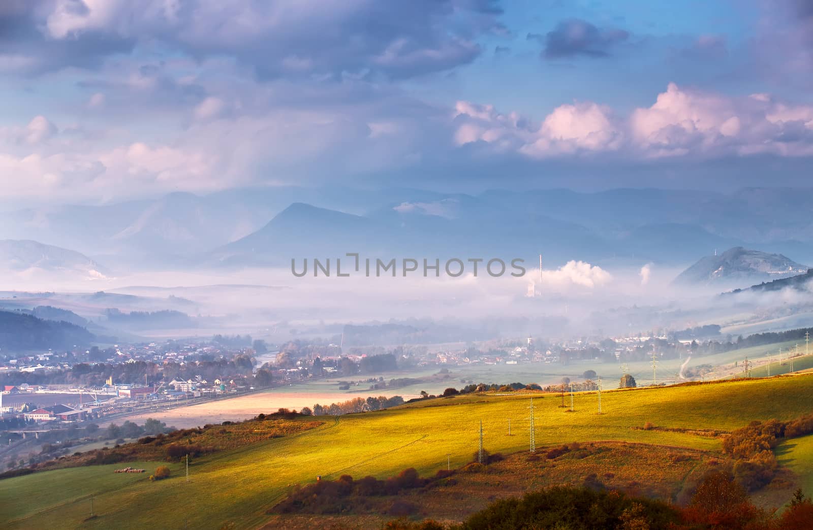 Foggy sunny morning in mountain village. Misty hills in Slovakia Tatras mountains. Town in valley.