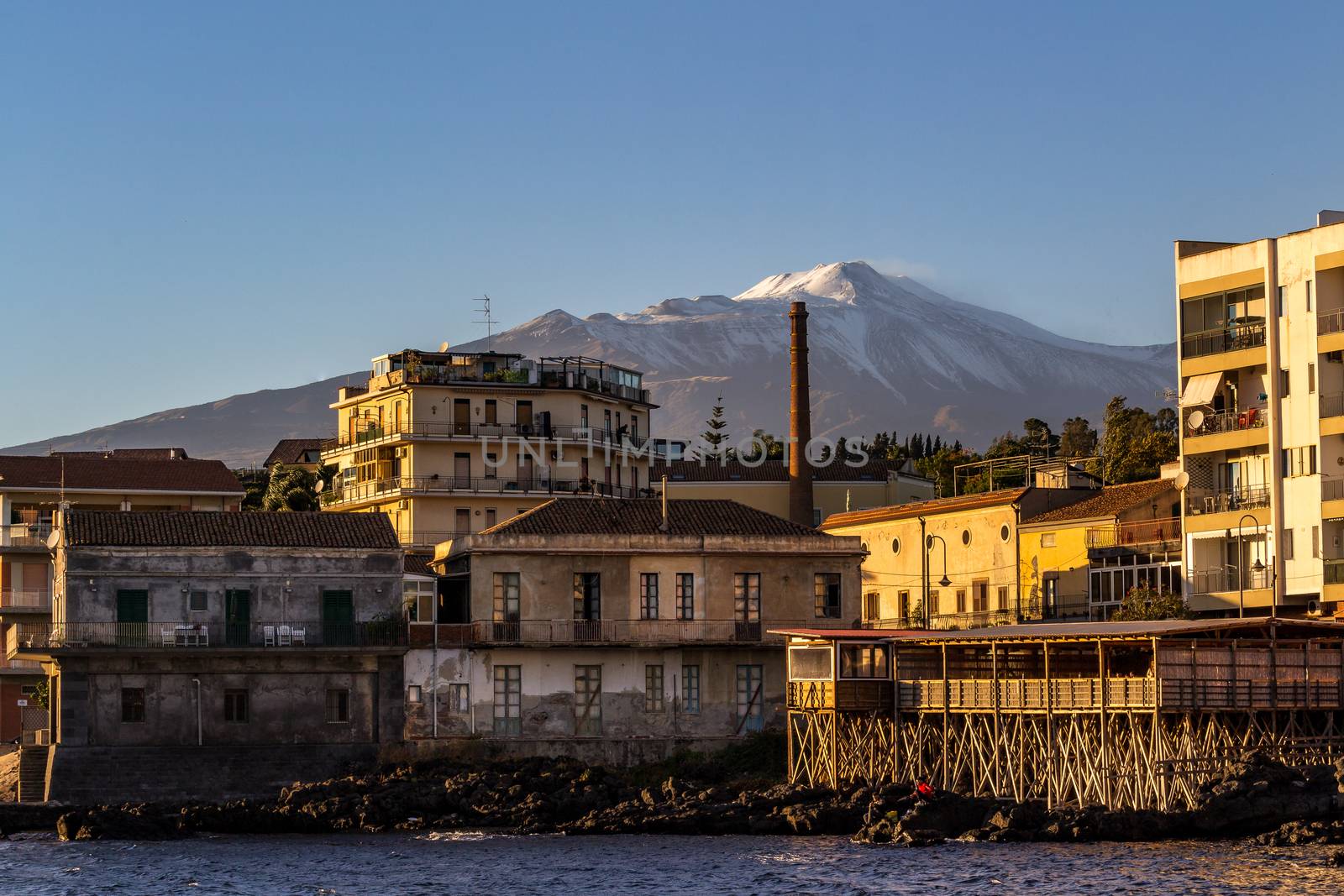 View of the volcano Etna from a small fishing village illuminated by the afternoon sun