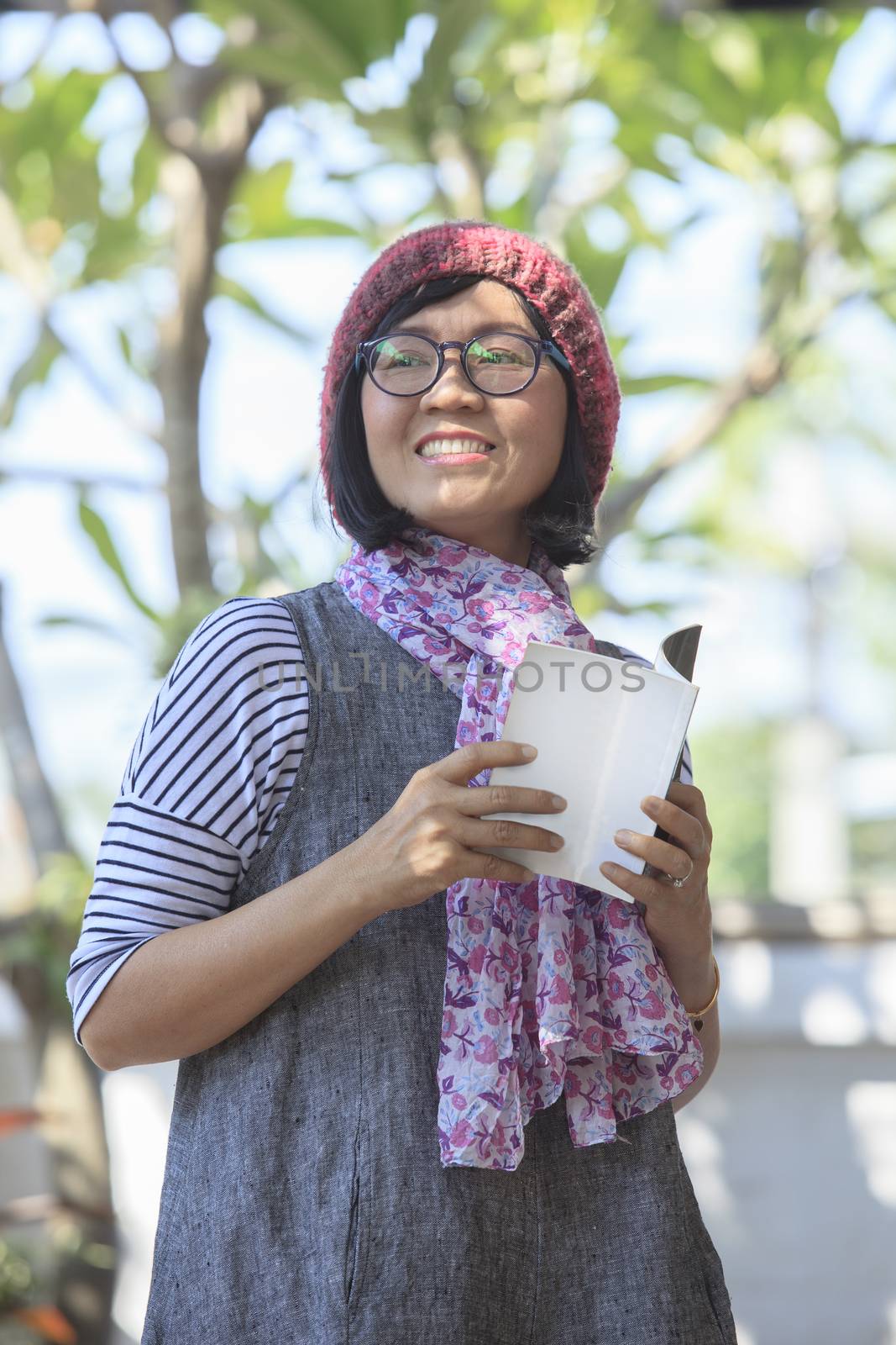 asian woman holding open booket book in hand and toothy smiling  by khunaspix