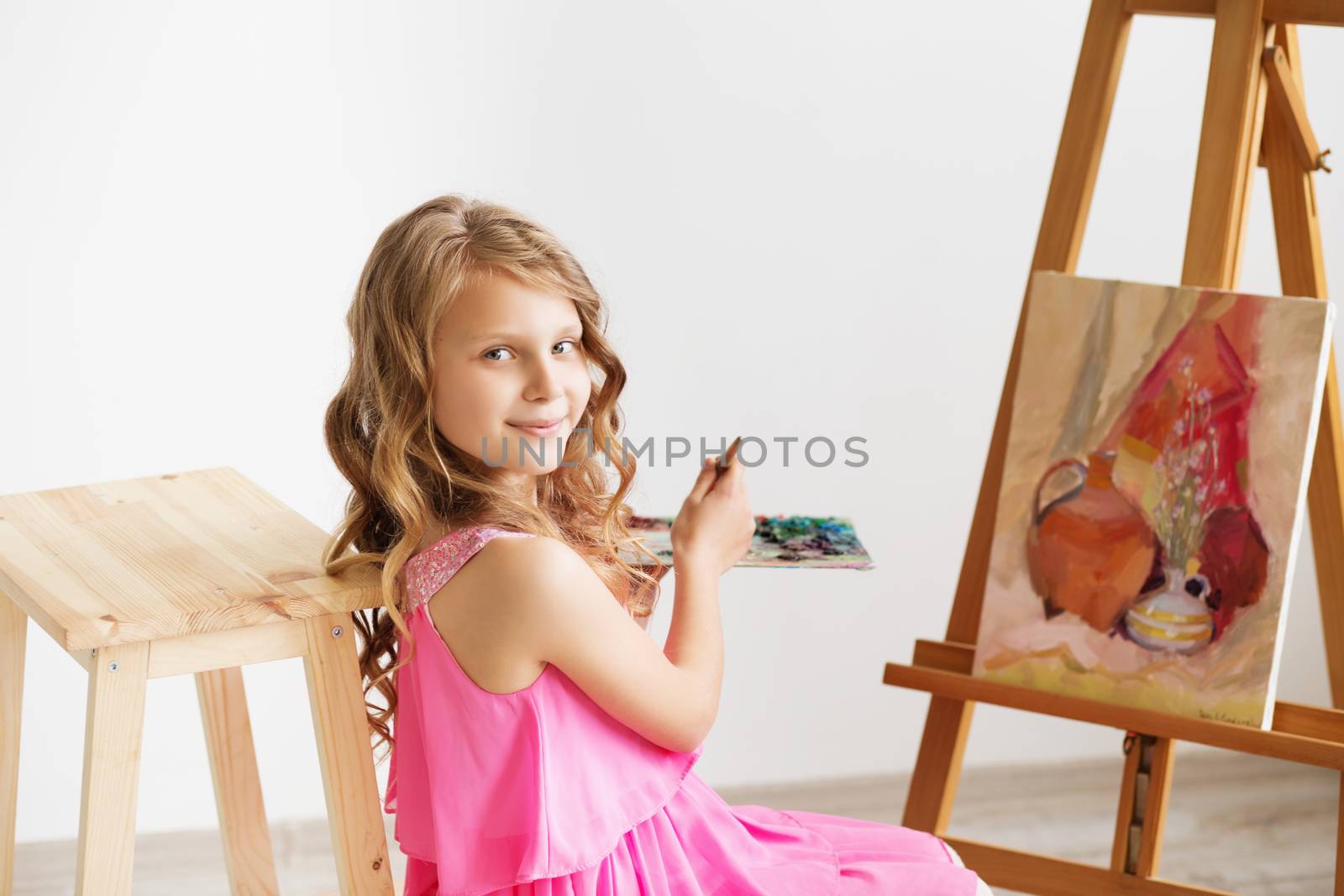Portrait of a lovely little girl painting a picture in a studio or art school. Creative pensive painter child paints a colorful picture on canvas with oil colors in workshop. Talented kids