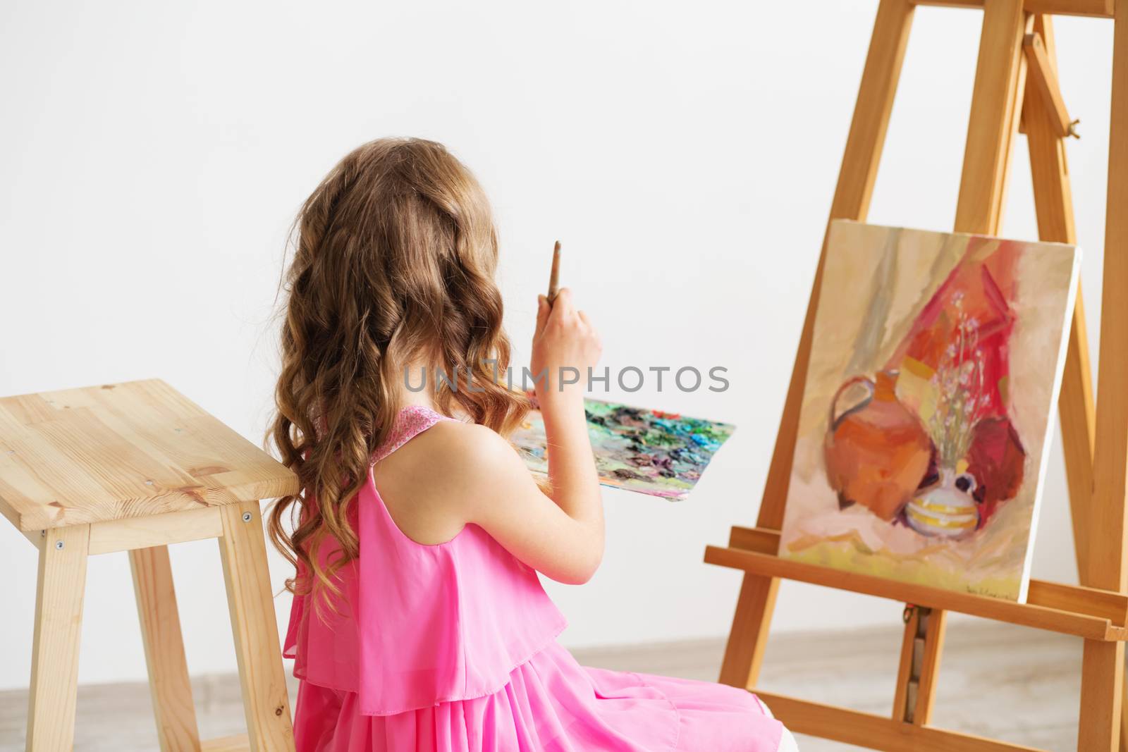 Portrait of a lovely little girl painting a picture in a studio or art school. Creative pensive painter child paints a colorful picture on canvas with oil colors in workshop. Talented kids