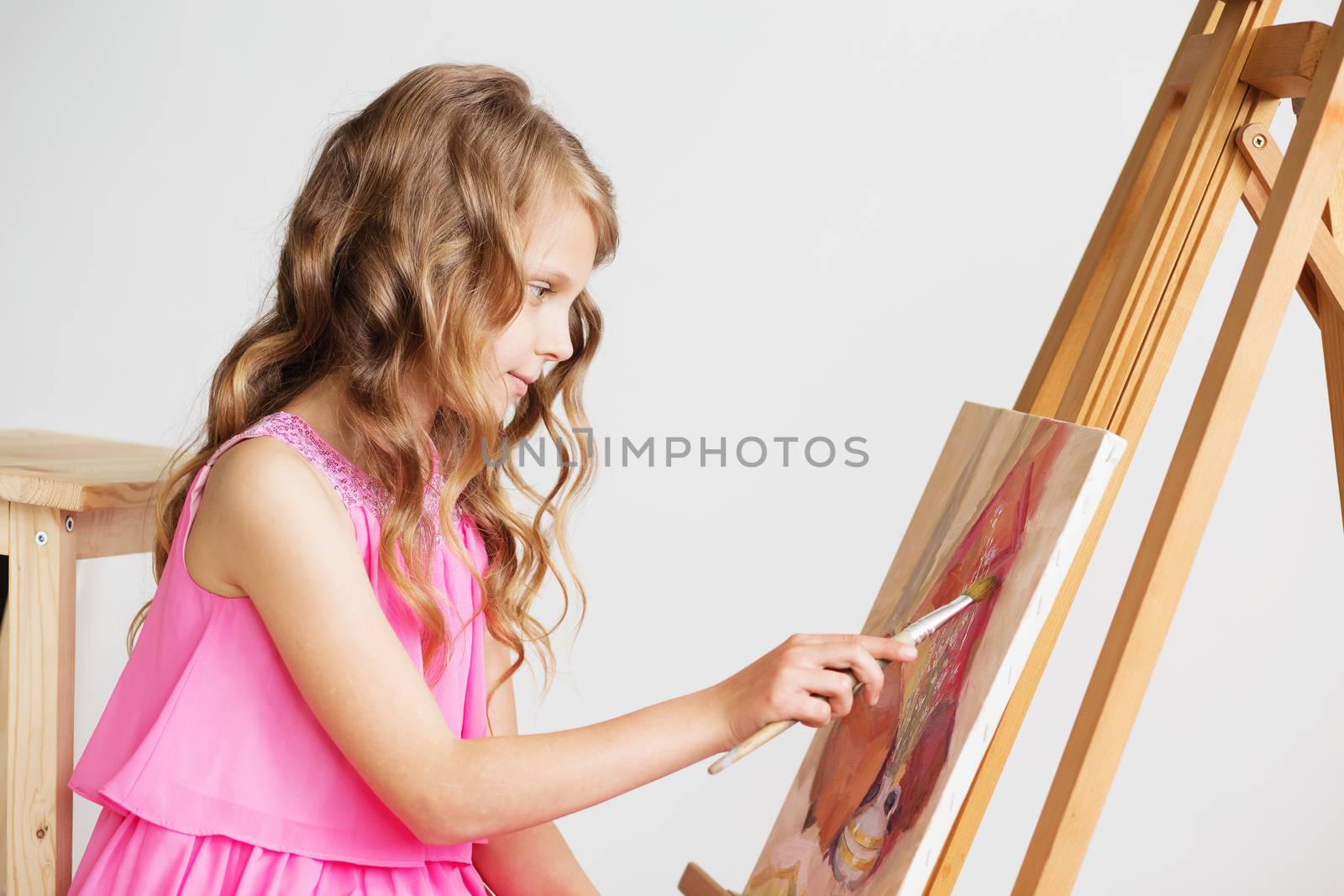 Portrait of a lovely little girl painting a picture in a studio or art school. Creative pensive painter child paints a colorful picture on canvas with oil colors in workshop. Talented kids