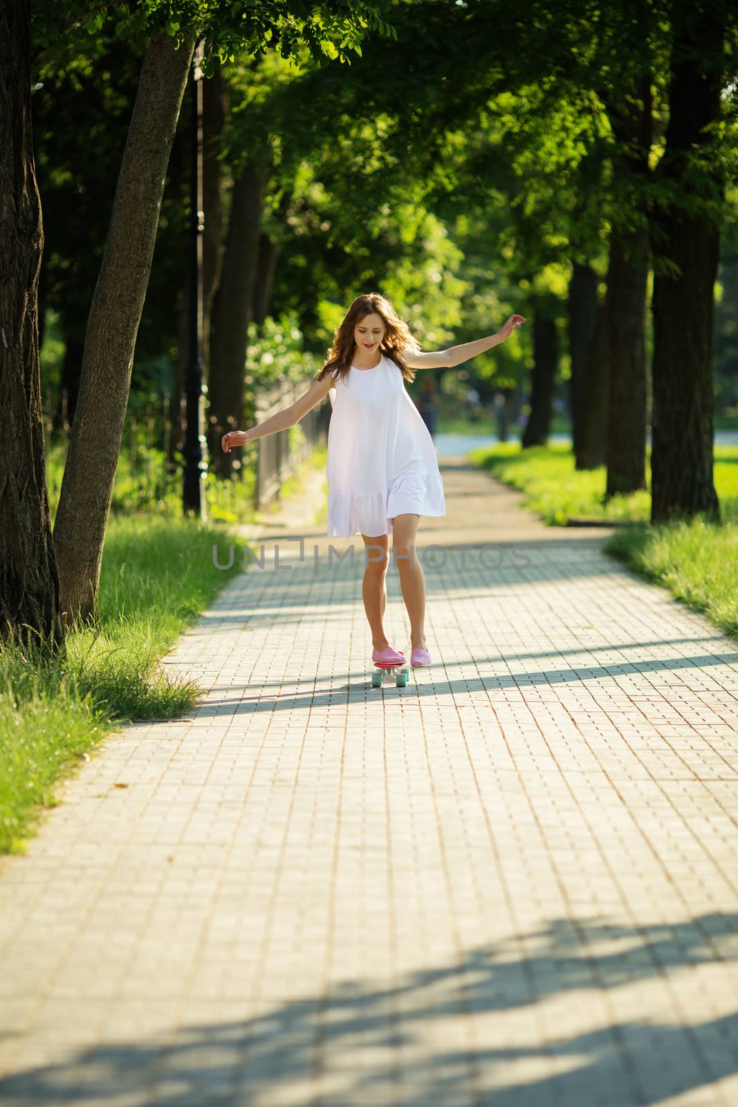 lovely urban woman in white dress with a pink skate. Young girl riding in the park on a skateboard