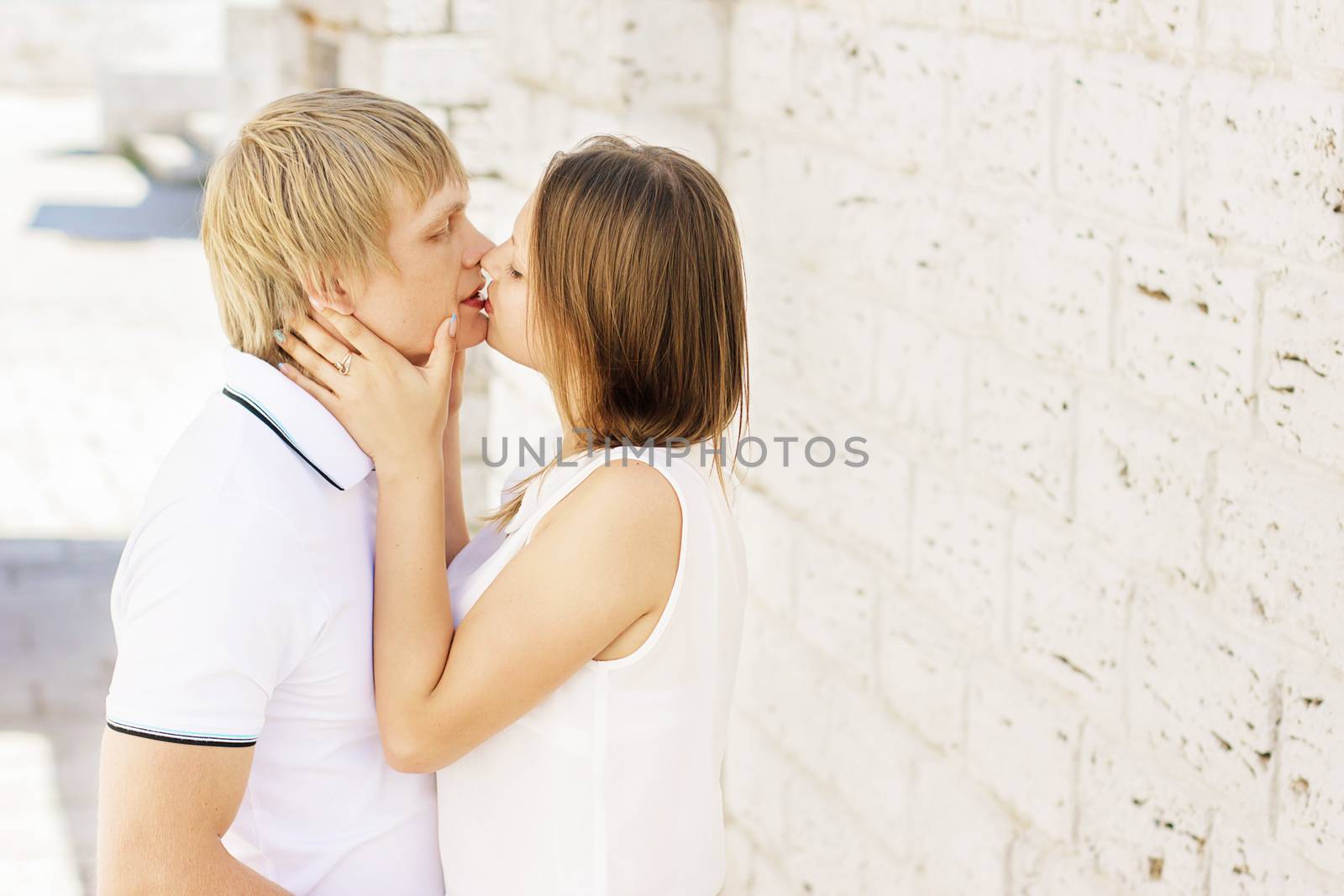 Man and woman kissing and embracing near the white brick wall on the street.