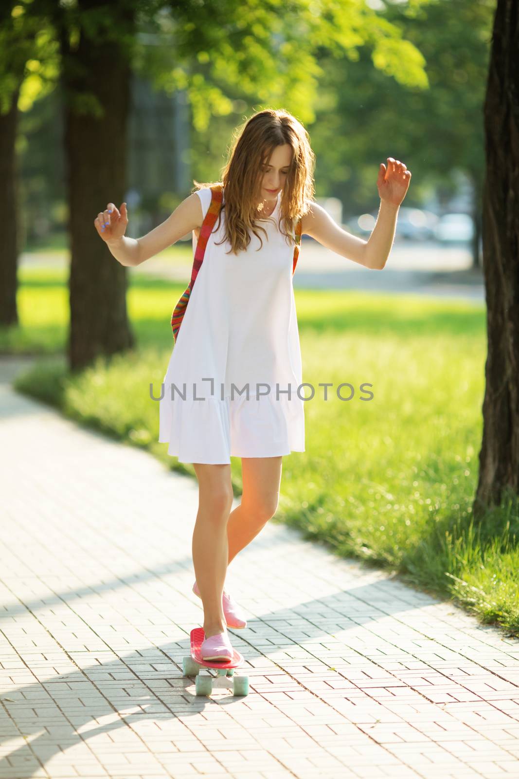 lovely urban woman in white dress with a pink skate. Young girl riding in the park on a skateboard