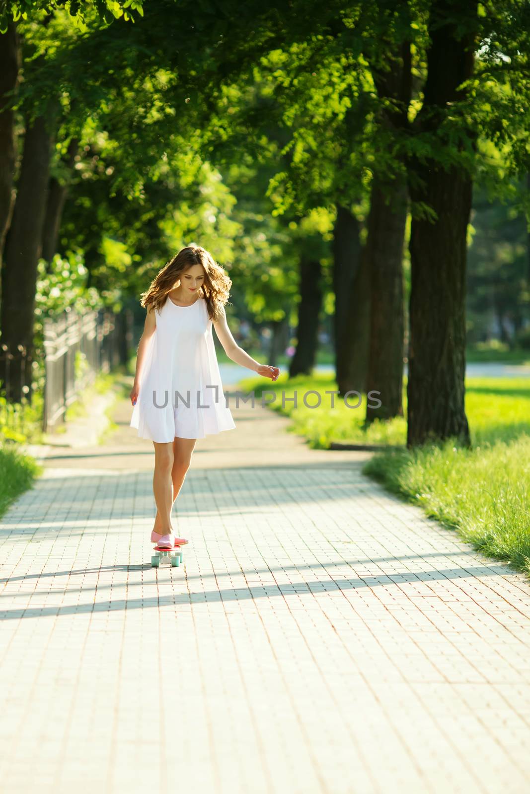 lovely urban woman in white dress with a pink skate. Young girl riding in the park on a skateboard