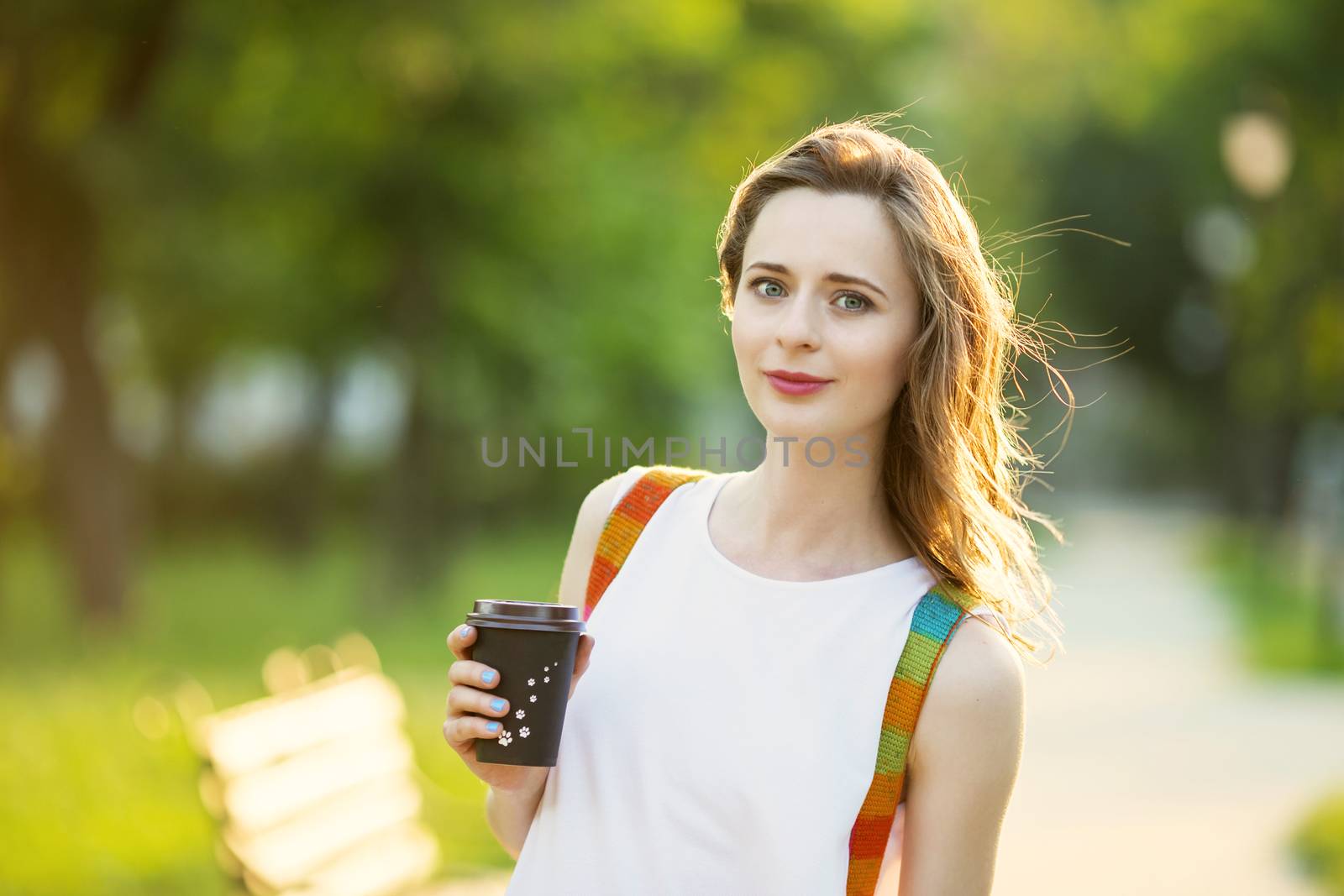 Portrait of lovely urban girl with paper cup in her hands. Happy smiling woman. Fashionable blonde girl walking in a city park