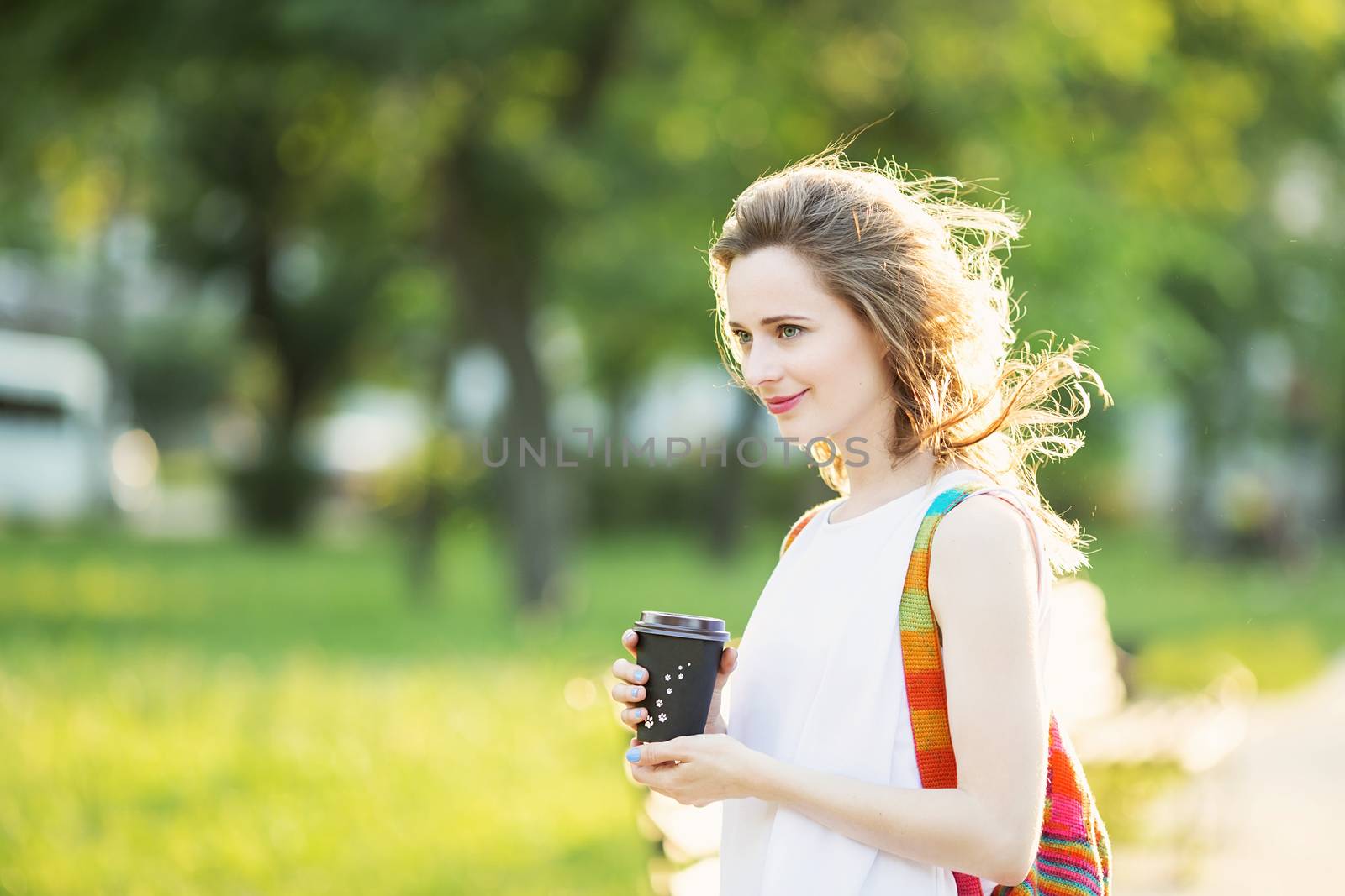 Portrait of lovely urban girl with paper cup in her hands. Happy smiling woman. Fashionable blonde girl walking in a city park