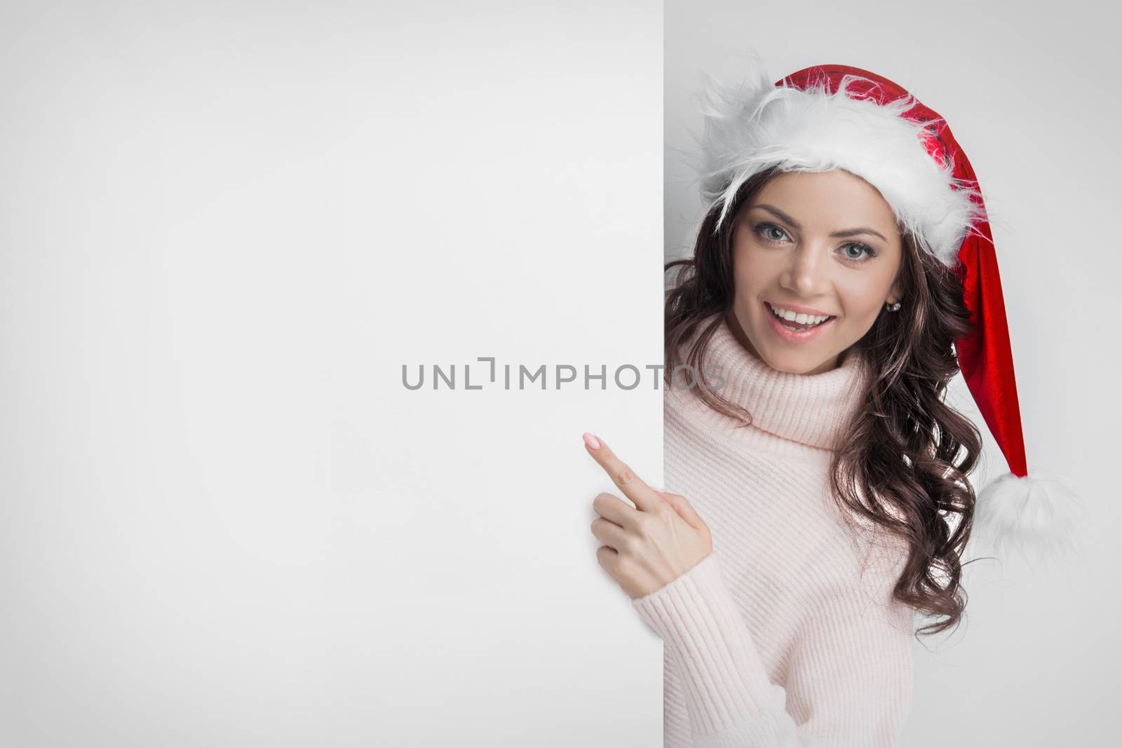 Woman in Santa's hat pointing at white copyspace