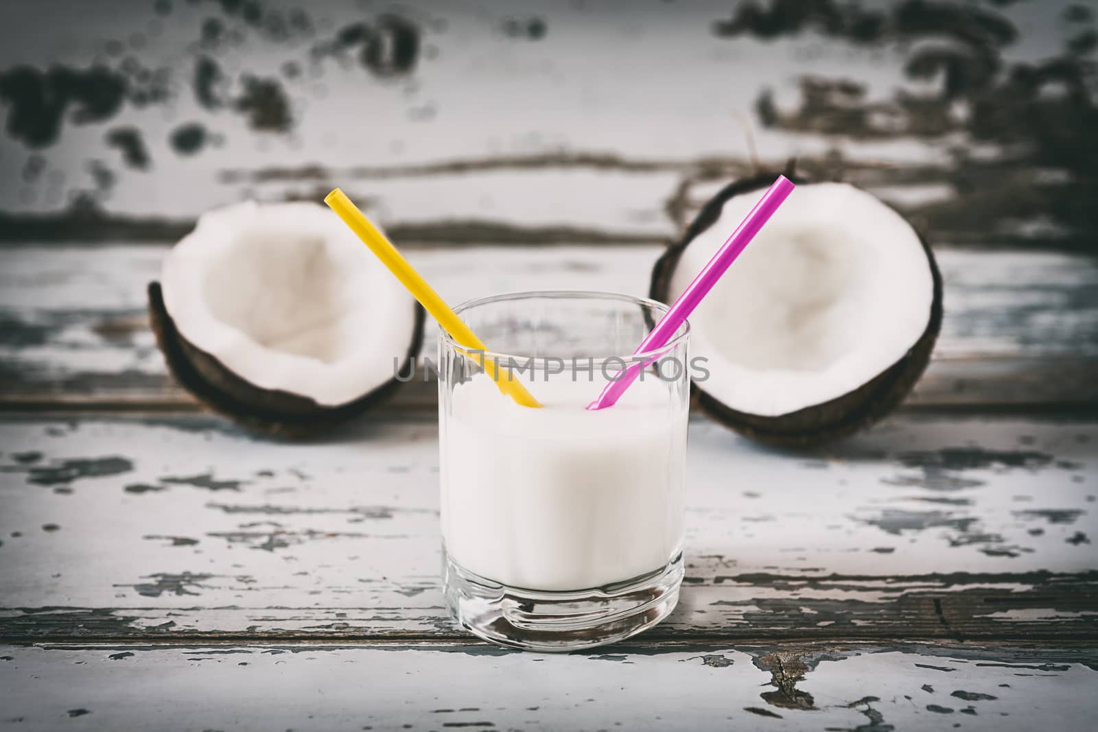Coconut milk in a glass with two straws over a wooden background