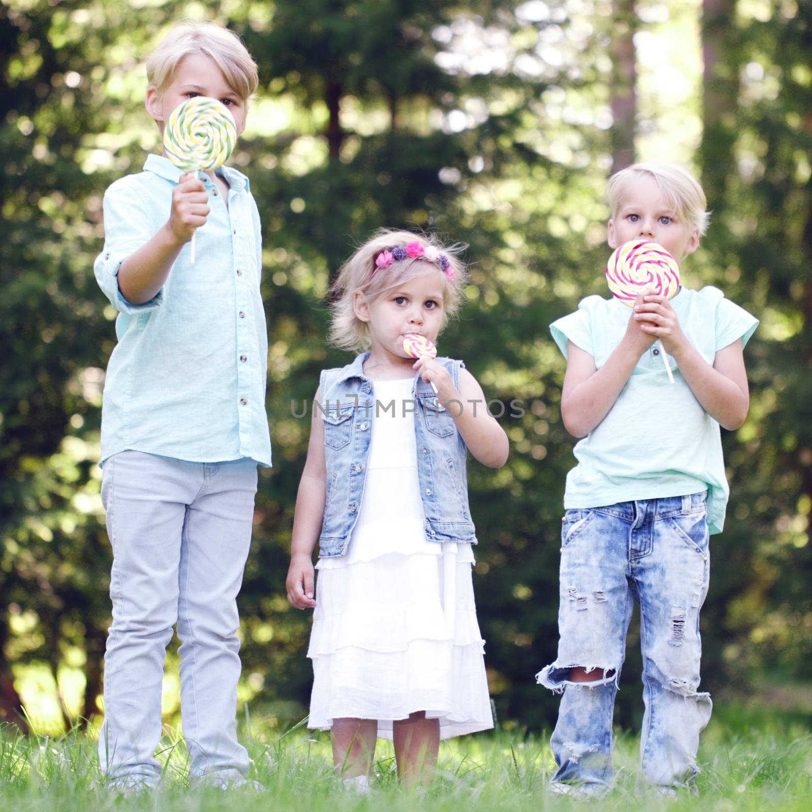 Group of happy children eating lollipops outdoors in summer park