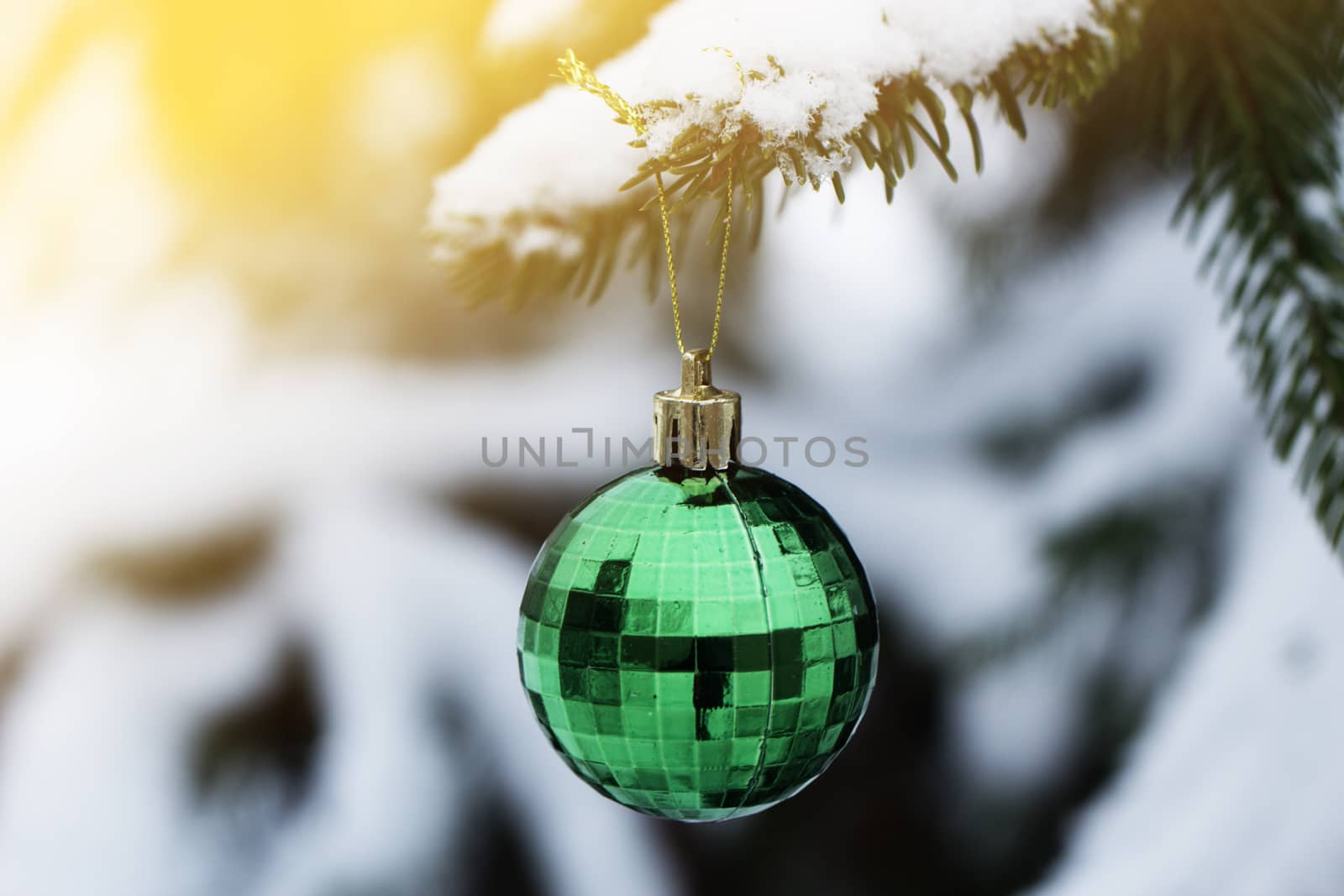 Green Christmas ball hanging on natural branch of pine in snowy weather.Christmas toy in the shape of a ball hanging on a spruce branch